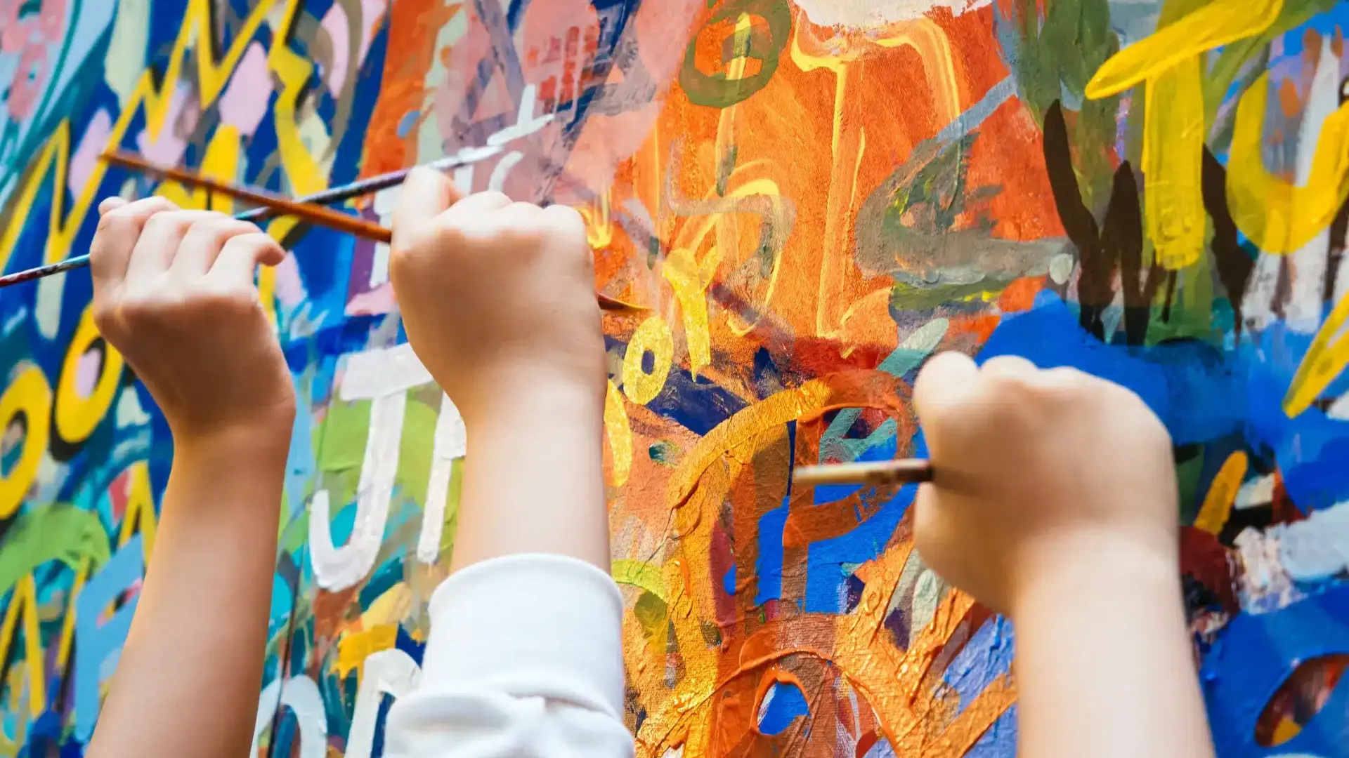 Kilka rąk z pędzlami malujących wspólnie kolorowe, ekspresyjne graffiti na dużym płótnie podczas urodzin w studio artystycznym.