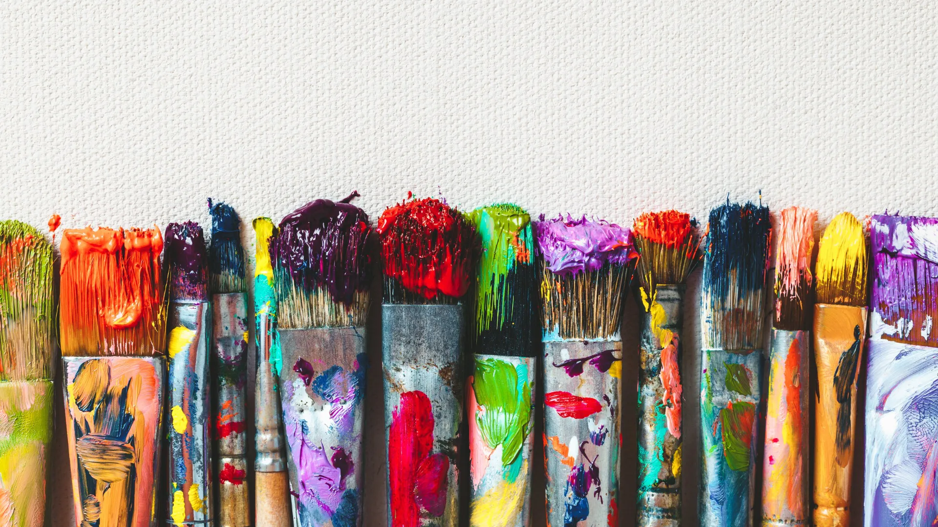 Szereg różnorodnych pędzli artystycznych ubrudzonych kolorowymi farbami, ustawionych pionowo na tle białego płótna, ilustrujący zasady korzystania z przyborów w Studio Pan Kleks.